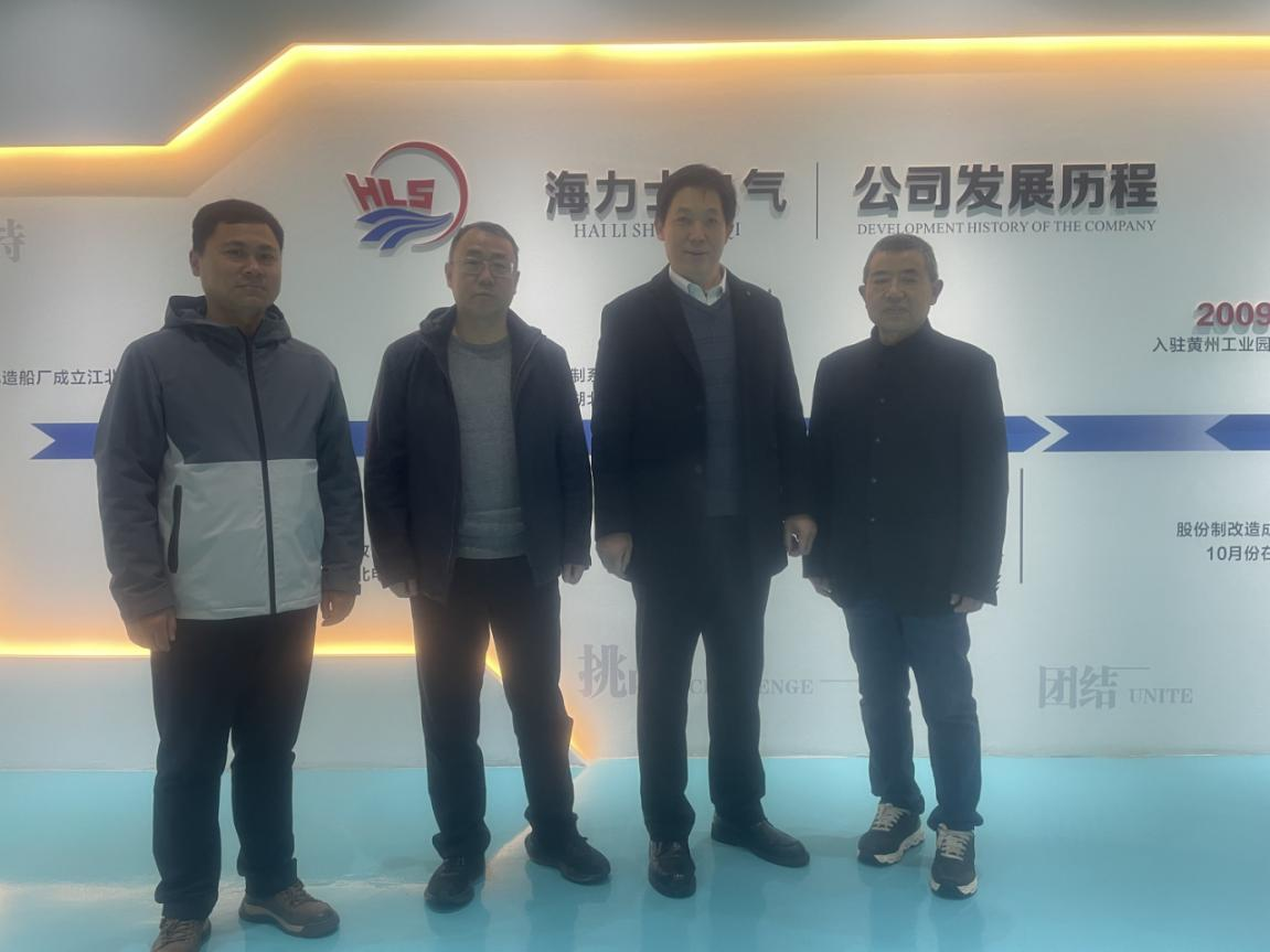 Фото: Делегация и руководители компании позируют для группового фото на фоне стены, посвященной истории развития компании.